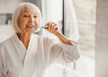 older woman smiling while brushing teeth 