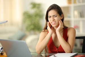 Woman in red shirt rubbing jaw in pain